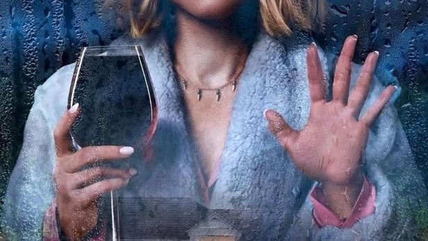 Kristen Bell hält ein Weinglas in der Hand, im Hintergrund das Cover von „The Woman in the House Across the Street From the Girl in the Window“.