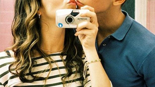 Ein Paar macht ein Selfie mit einer Kompaktkamera, während sie sich gegenseitig einen Kuss geben.