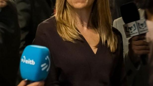 Eine Frau wird von Reportern umringt, im Vordergrund Mikrofone.