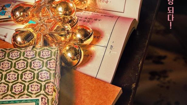 Ein goldener Glockenanhänger liegt auf einem aufgeschlagenen Buch mit koreanischer Schrift.