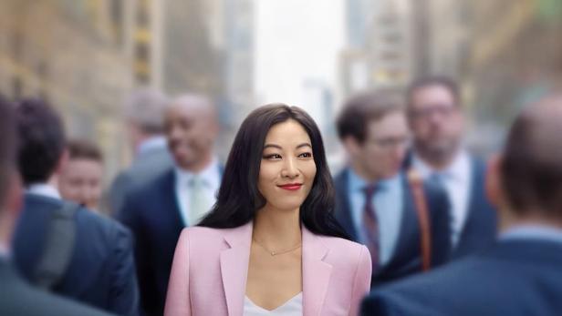 Eine Frau im pinkfarbenen Hosenanzug geht mit ihrem Handy in der Hand durch eine Menschenmenge.