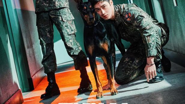 Zwei Militärpolizisten posieren mit einem Dobermann in einem Flur.