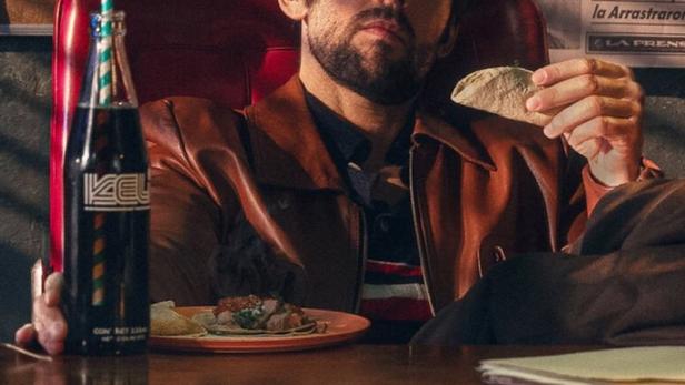 Der Detektiv Belascoarán isst Tacos in seinem Büro, im Hintergrund eine Wand voller Zeitungsartikel.