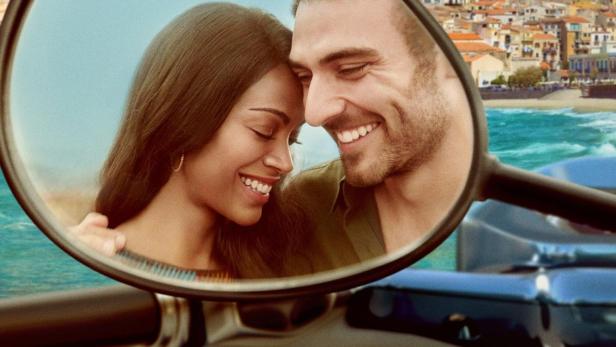 Ein Paar umarmt sich, gesehen im Spiegel eines Motorrollers vor einer Küstenstadt.