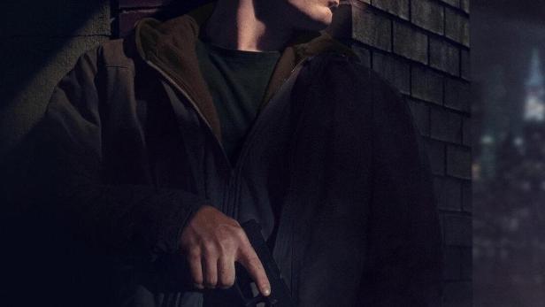 Ein Mann mit einer Waffe steht im Dunkeln an einer Ziegelwand.