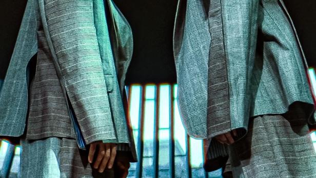 Zwei Männer in Anzügen stehen Stirn an Stirn vor einem dunklen Hintergrund.