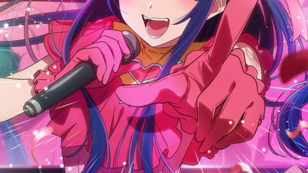 Ein Anime-Mädchen im pinkfarbenen Idol-Kostüm singt mit einem Mikrofon auf der Bühne.