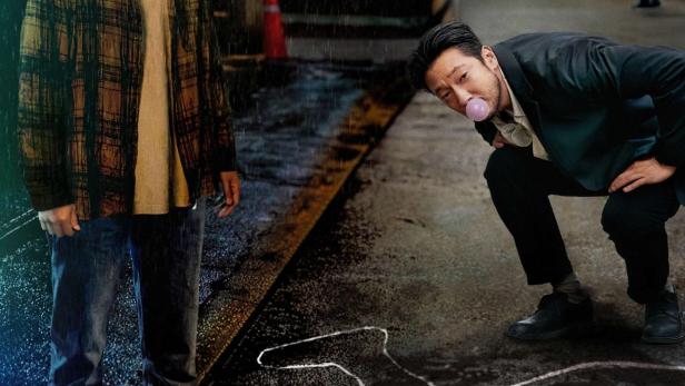 Ein Mann steht im Regen neben einer Tatortmarkierung, während ein Detektiv Kaugummi kaut.