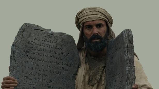 Ein Mann, dargestellt als Moses, hält zwei Steintafeln mit Inschriften.