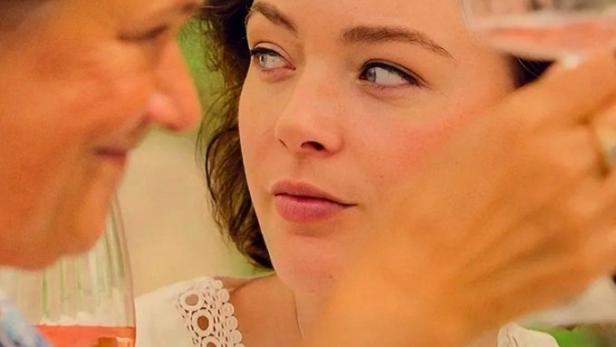 Eine Frau mit Blumenkranz prostet einer anderen Frau mit einem Glas Roséwein zu.