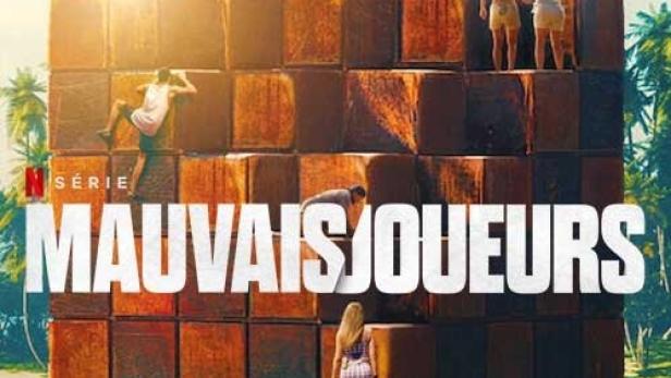 Das Poster für die Netflix-Serie „Mauvais Joueurs“ zeigt Menschen auf einem Würfelgebäude vor einem Strand.
