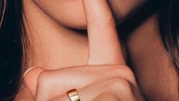Eine Frau mit rotem Lippenstift hält einen Finger an ihre Lippen.
