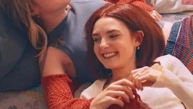 Drei junge Frauen liegen lachend auf einem gemusterten Teppich.