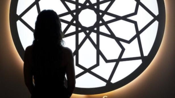 Eine Frau steht vor einem beleuchteten, geometrischen Muster, das an ein Netflix-Logo erinnert.