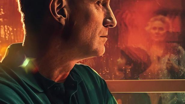 Ein Mann blickt aus dem Fenster, im Hintergrund ist eine verschwommene Frauengestalt zu sehen.