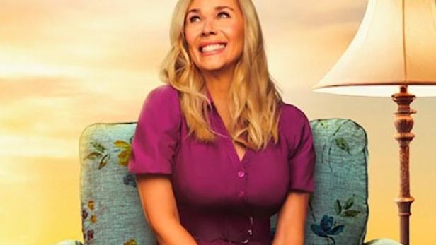 Eine Frau sitzt in einem blumengemusterten Sessel vor einem Sonnenuntergang.