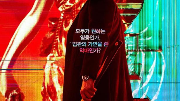 Ein Mann im Mantel hält einen Hammer vor einem roten und blauen Hintergrund für die Serie „The Devil Judge“.