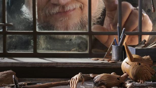 Guillermo del Toro hinter einem Fenster, darunter eine Pinocchio-Puppe aus Holz.