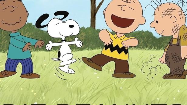 Die Peanuts-Charaktere tanzen auf einer Wiese vor einem Baum, auf dem Woodstock sitzt.