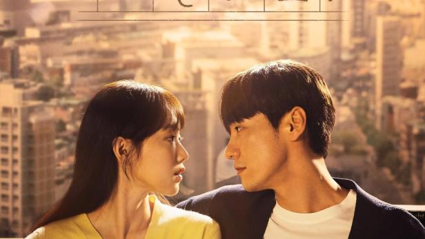 Ein Mann und eine Frau sitzen vor einem Fenster mit Blick auf eine Stadt.