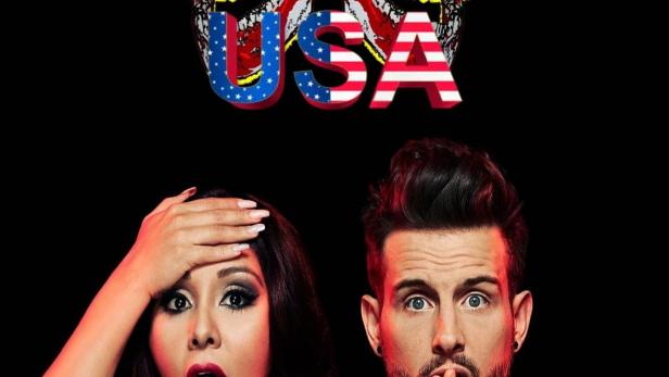 Werbeplakat für „Just Tattoo Of Us USA“ mit zwei überrascht aussehenden Moderatoren vor Schädeln mit US-Flaggenmuster.