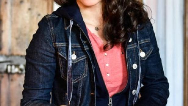 Eine Frau mit lockigem Haar und Jeansjacke hält eine Karte in der Hand.