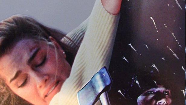 Eine Frau klammert sich ängstlich an einen Pfeiler, während ein Mann mit einer Axt im Dunkeln lauert.