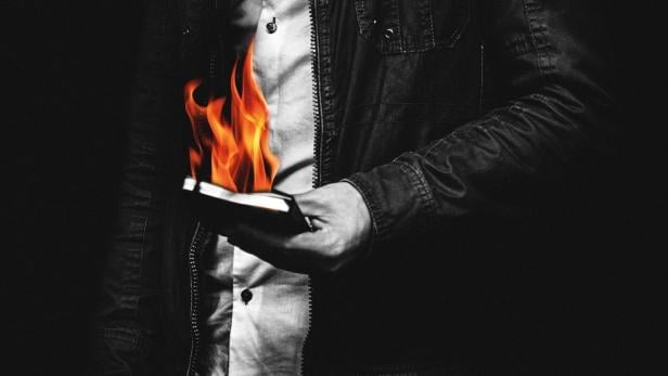 Ein Mann hält ein brennendes Buch in der Hand.