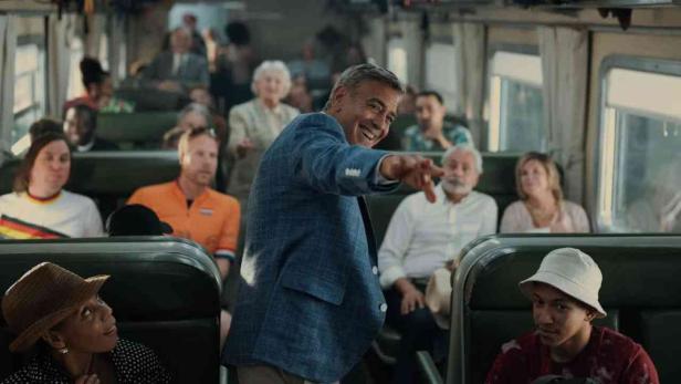 George Clooney zeigt in einem Zug auf etwas.