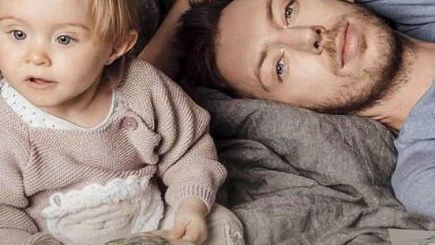 Ein Mann liegt mit einem kleinen Kind auf dem Bett.