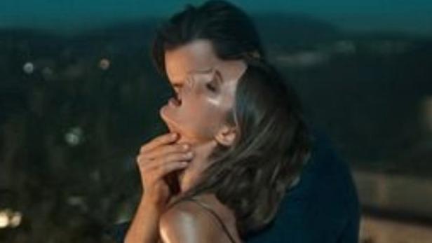 Ein Paar umarmt sich innig vor einer nächtlichen Stadtkulisse.