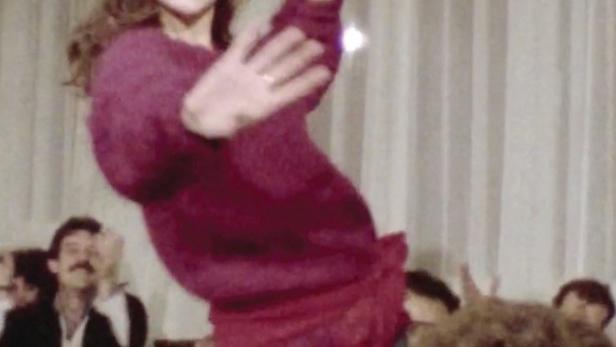 Eine junge Frau tanzt auf einem Tisch, umgeben von Zuschauern.