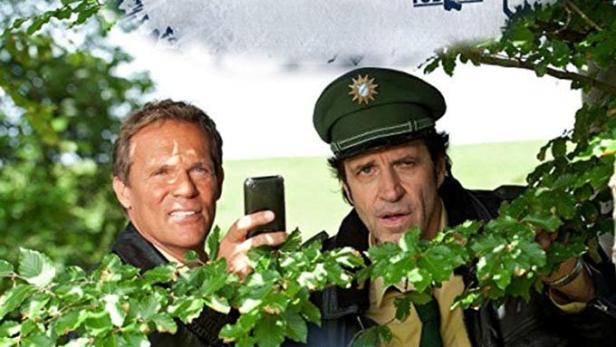 Das Filmplakat zur Serie „Hubert und Staller“ zeigt die beiden Hauptdarsteller hinter Ästen.