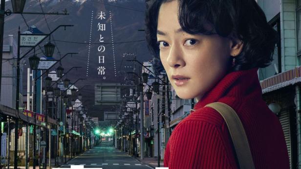 Eine Frau blickt über die Schulter, während ein UFO über eine japanische Stadt fliegt, im Hintergrund der Berg Fuji.