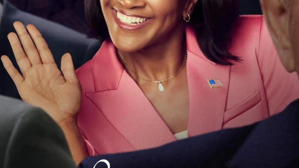 Eine lächelnde Frau im pinkfarbenen Blazer mit einer US-Flagge am Revers winkt.