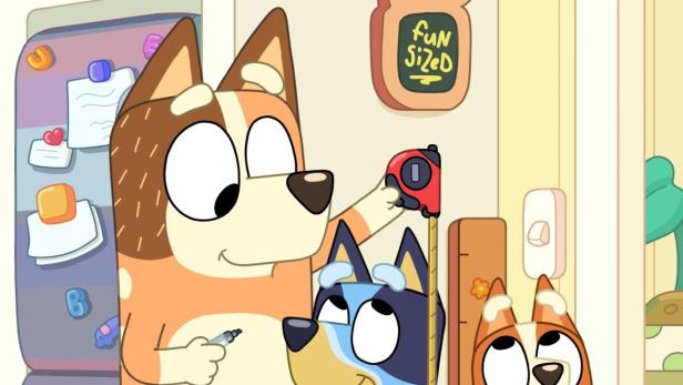 Die animierten Hunde Bluey, Bingo und Bandit messen sich an einer Wand.