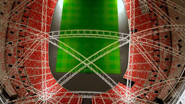 Luftaufnahme eines Stadions mit roter Bestuhlung und einem grünen Spielfeld.