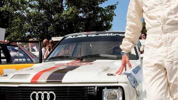 Walter Röhrl posiert neben einem weißen Audi Quattro Rennwagen.
