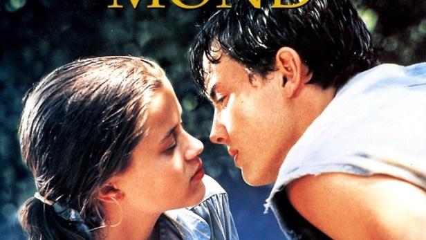 Das Filmplakat für „Der Mann im Mond“ zeigt ein junges Paar und eine Person auf einer Wiese.