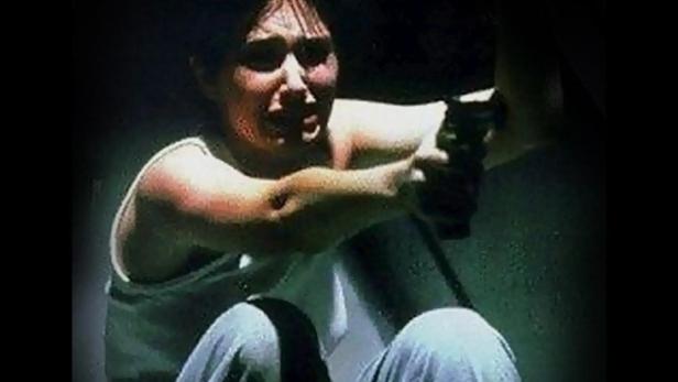 Ein verletzter Mann zielt mit einer Pistole in der Dunkelheit.