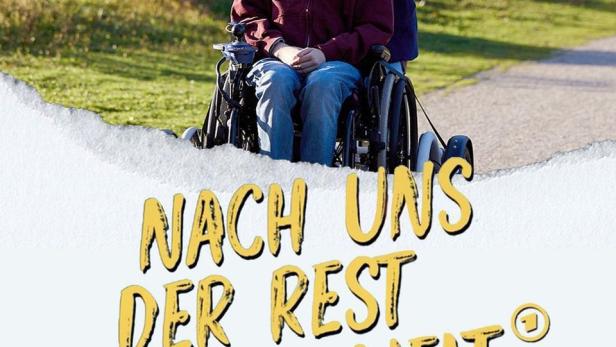 Ein junger Mann im Rollstuhl wird von einer jungen Frau in einem Park geschoben. Unten liegt ein Mädchen im Gras.