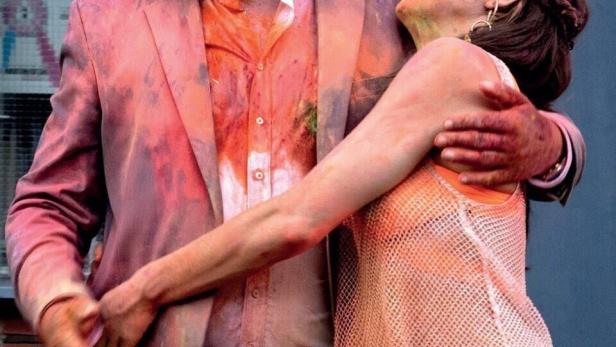 Ein Mann und eine Frau, beide mit Farbflecken bedeckt, umarmen sich.