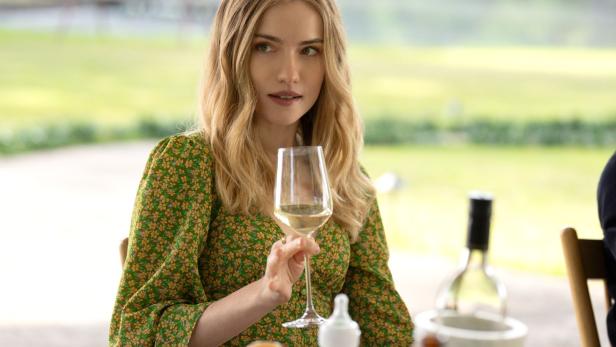 Eine Frau im geblümten Kleid hält ein Glas Weißwein in der Hand.