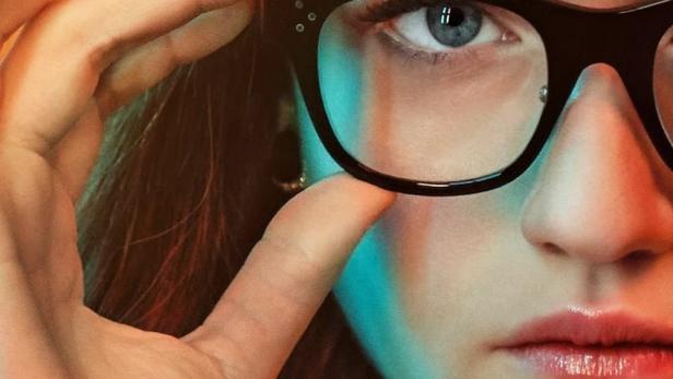 Das Filmplakat von „Inventing Anna“ zeigt Julia Garner mit Handschellen und einer großen Brille.