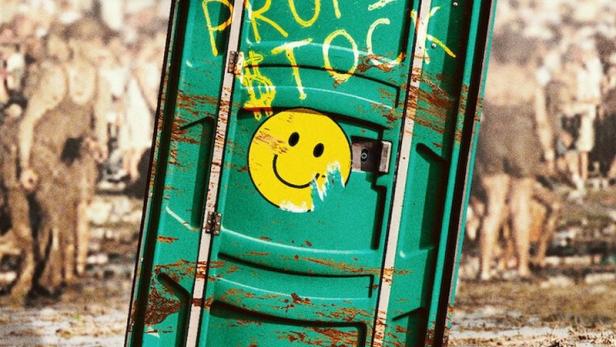 Ein Dixi-Klo mit der Aufschrift „End Profitstock“ steht in Flammen, im Hintergrund eine Menschenmenge.