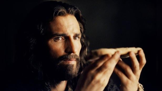 Ein Mann mit Bart hält ein Stück Brot in seinen Händen.