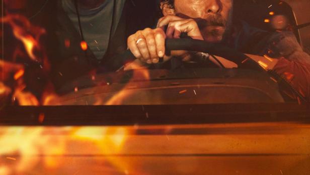 Ein Mann und eine Frau sitzen ängstlich in einem Bus, umgeben von Flammen.