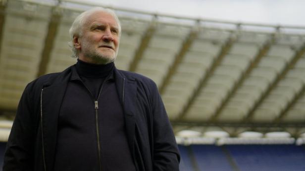 Rudi Völler steht in einem Stadion und blickt nach oben.