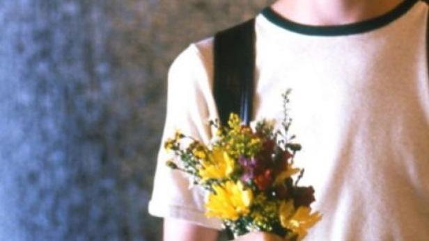 Ein junger Mann mit Sommersprossen hält einen bunten Blumenstrauß.