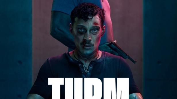 Ein Mann mit Handschellen sitzt auf einem Stuhl, während ein älterer Mann mit einer Waffe hinter ihm steht. Titel: „Turm Schatten“.